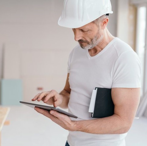 Uomo con casco di protezione che utilizza un tablet all'interno di un cantiere