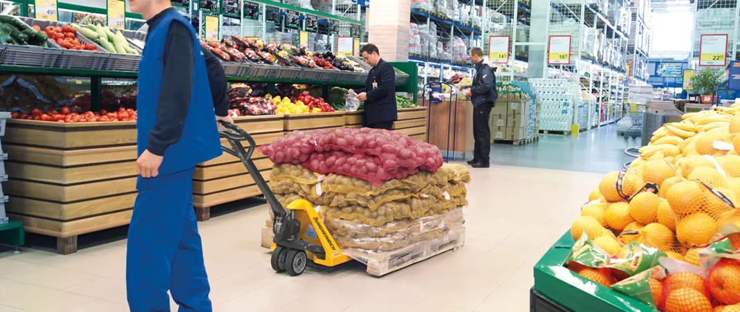 Ein Mann zieht einen beladenen Hubwagen durch ein Lebensmittellager